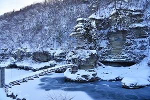 冬の塔のへつりの写真001（一面雪に覆われた岩肌や川の上のつり橋の様子）